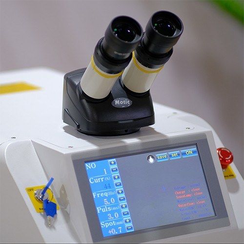 Touch control panel showing current, frequency, pulse width and spot settings, with the microscope above