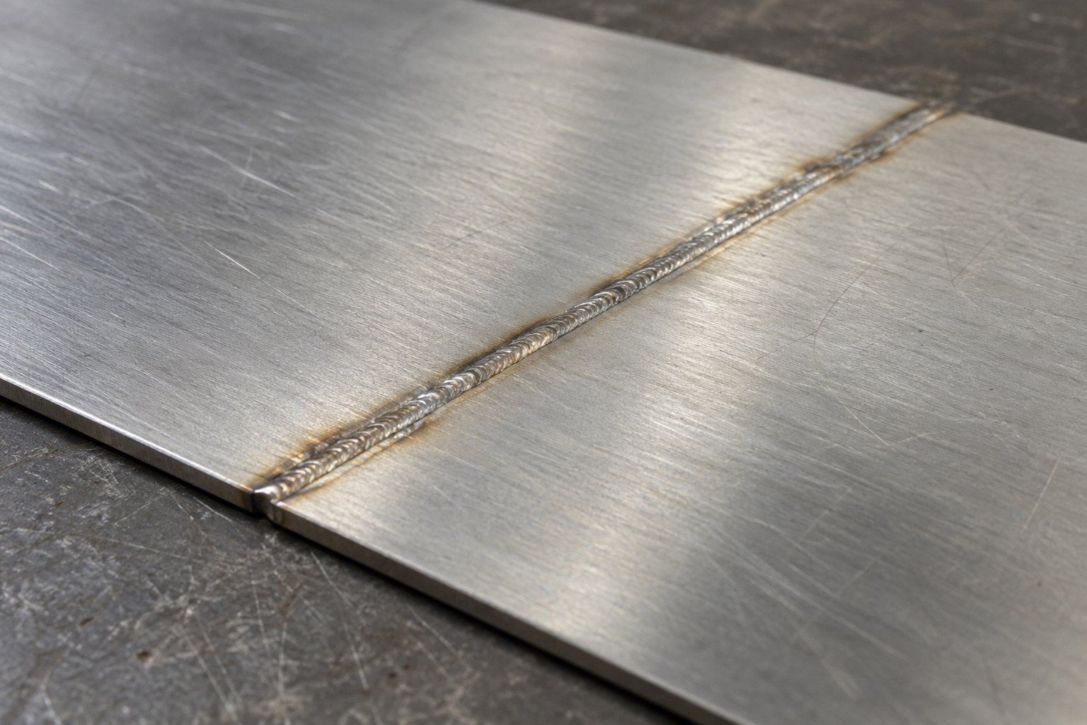 Narrow rippled laser weld bead joining two thin brushed stainless steel sheets, with light heat tint on both sides